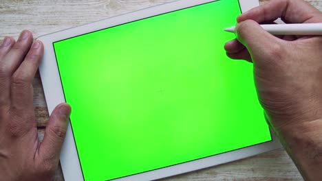 hombre escribiendo en una tableta con pantalla verde llave de croma en la mesa con bolígrafo