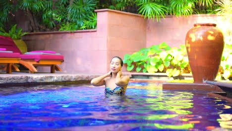 Sexy-Mujer-Asiática-Tocando-El-Cabello-Y-Alisando-Su-Cabello-Dentro-De-La-Piscina-En-El-Exótico-Salón-Del-Hotel-Tropical