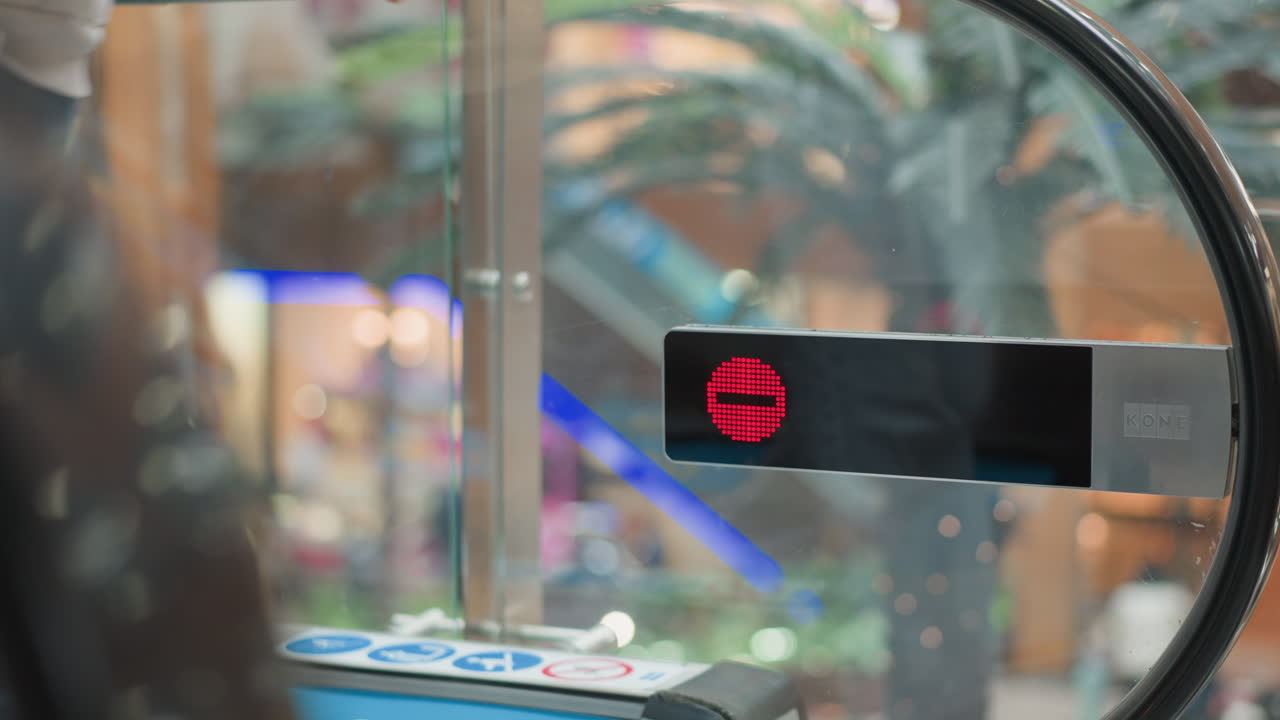 red stop indicator display mounted on glass panel of moving walkway while shopper steps off onto mall corridor with blurred pedestrian and vibrant store front lighting in modern mall background