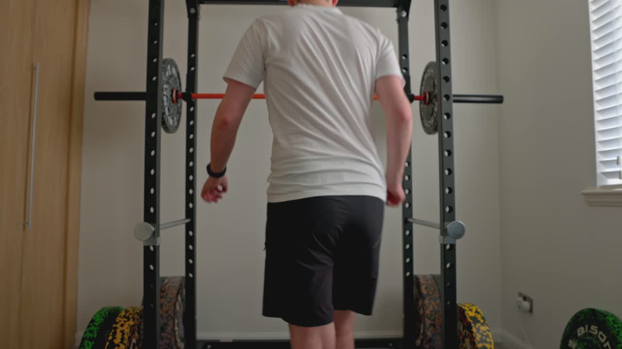 una ripresa statica di un giovane che si sta posizionando giusto pronto per lo squat con il barbell