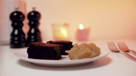 Sabroso-Desierto-Romántico:-Brownies-Con-Compota-De-Manzana-En-Un-Plato-Blanco-Con-Velas-En-El-Fondo