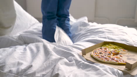 people jumping on bed next to cardboard with half pizza and french fries with ketclup