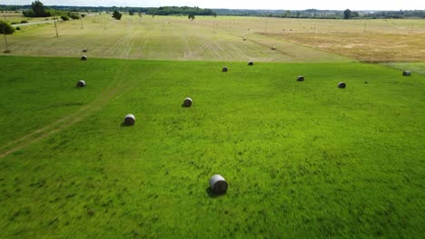 aerial view hay bales in the green agriculture field, bailed hay drying on ranch land, the straw is compressed into roles, sunny summer day, wide drone shot moving forward