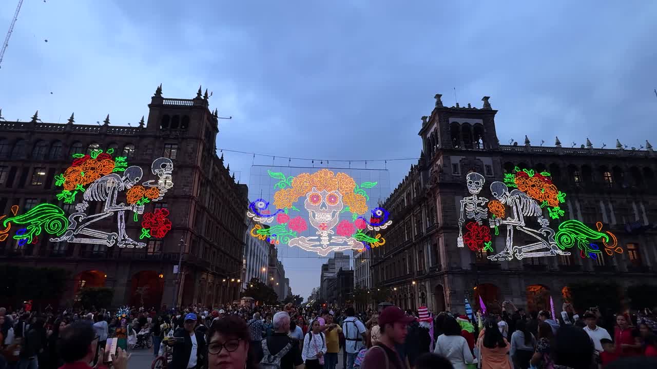 Illuminated Skeleton art on buildings at Zócalo square with people on day of the Dead