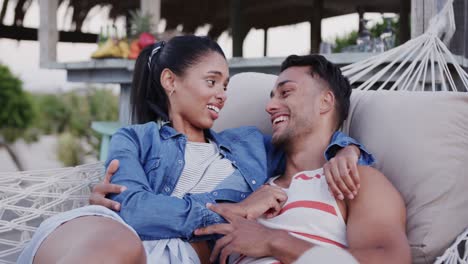 happy diverse couple relaxing in hammock together and talking at beach bar, in slow motion