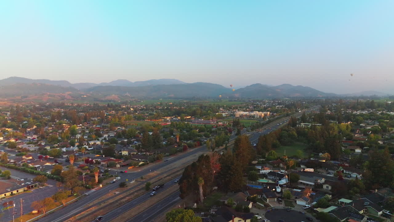 Roads full of cars in Napa, California, USA. Hot air balloons in the air over the city. Mountains at backdrop. Top view.