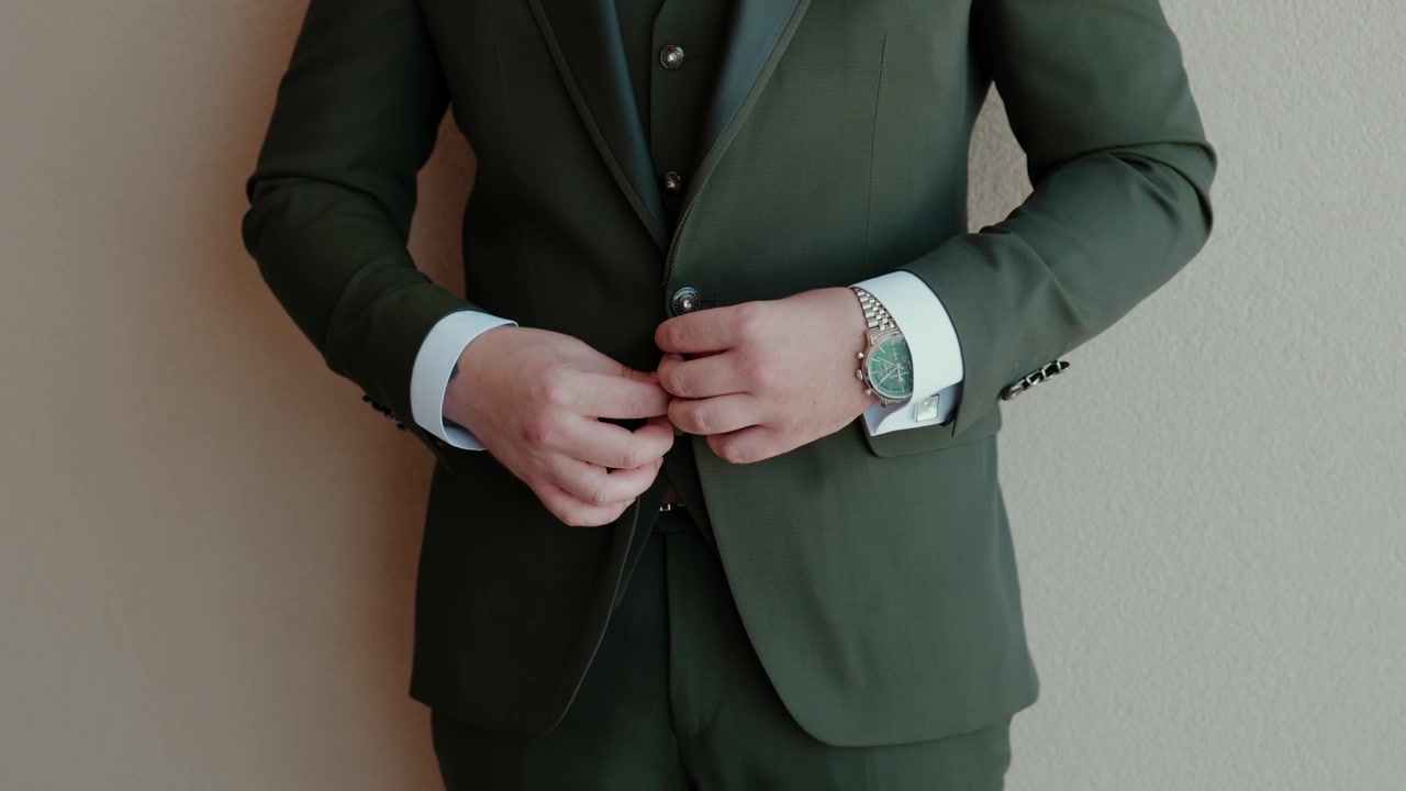 Sposo che abbottona la sua elegante giacca da abito verde scuro, preparandosi per il giorno del matrimonio o per un evento formale di lavoro