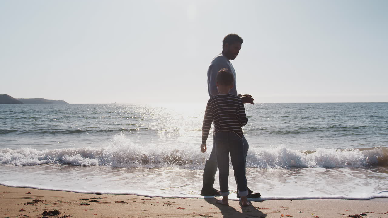 padre e hijo caminando por la playa rompiendo olas en la playa recogiendo piedras