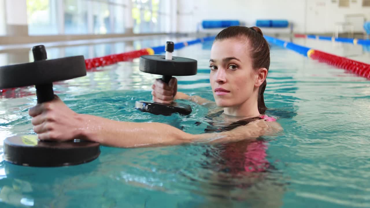 mujer en forma haciendo ejercicio con pesas de espuma en la piscina