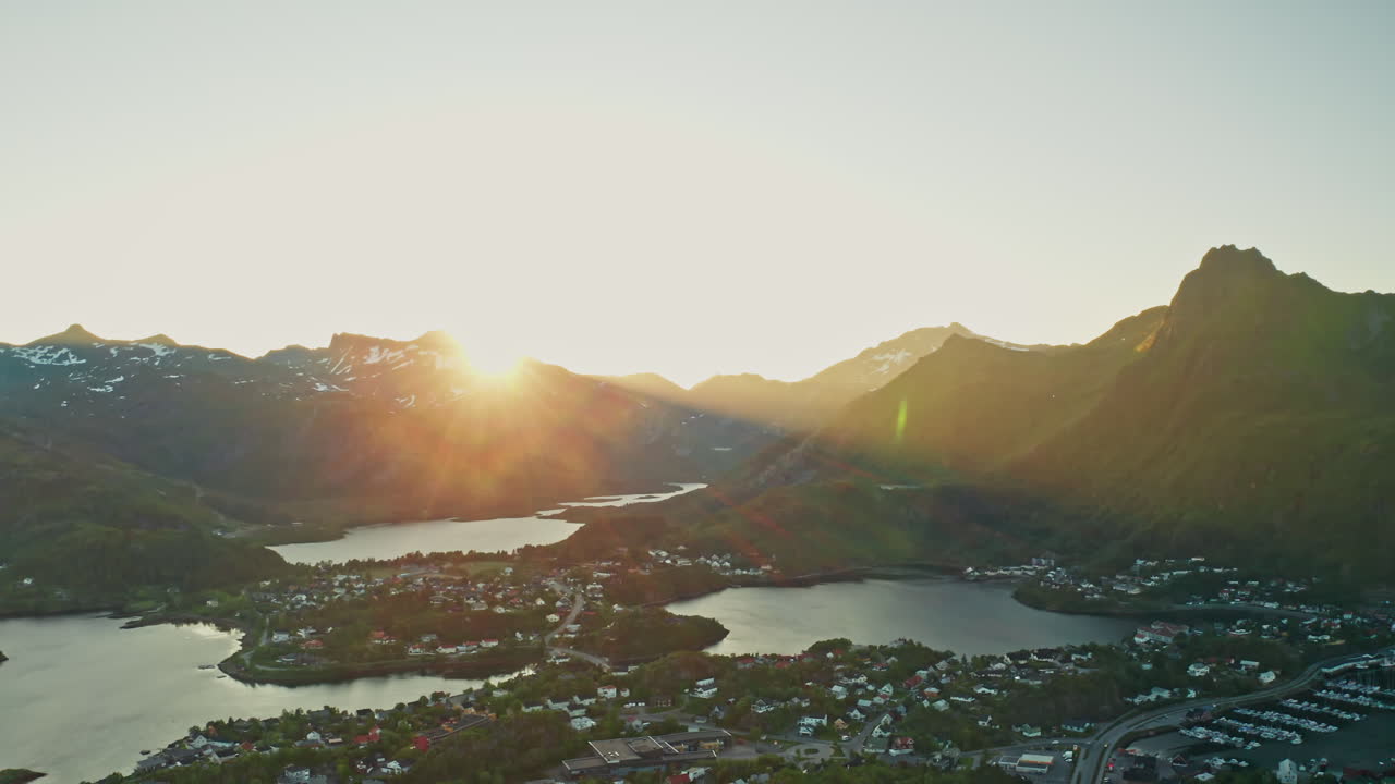 Aerial drone shot over the Norwegian town of Svolvaer in the Lofoten Islands, Norway. Bird's eye view of the fishermen's town at the midnight sun. View of the vast mountains in the background.