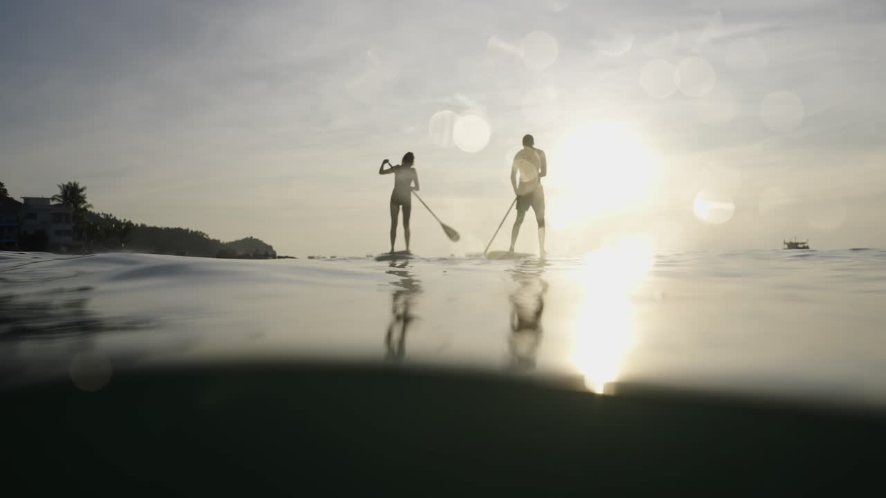 Silhouetted Couple Paddleboarding on Tranquil Water at Sunset
