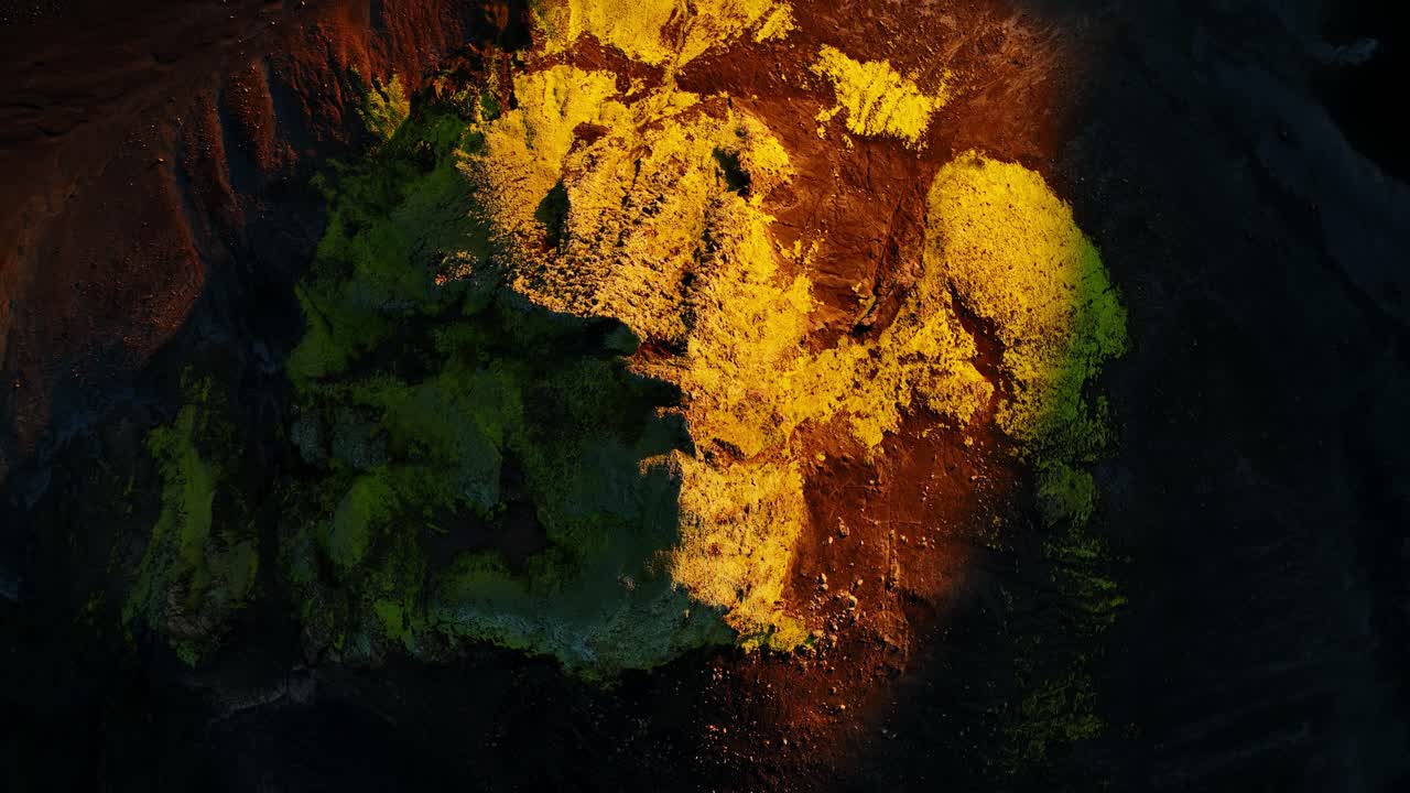 Vista aerea da drone di licheni gialli e muschio verde su sabbia vulcanica nera negli altopiani islandesi all'alba durante l'ora d'oro, creando una texture astratta suggestiva con ombre lunghe