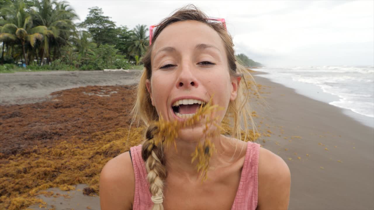 chica lúdica en la playa haciendo bigote con algas y luego riéndose de su broma tonta. la gente alegría jugando disfrutando de la vida en la naturaleza