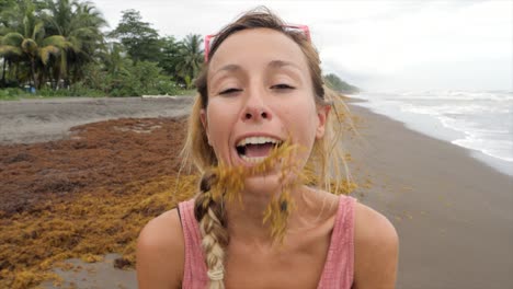 playful cool girl on beach making moustache with algae then laughing from her silly joke. people joy playing enjoying life in nature