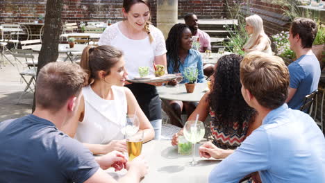 group of friends meeting for drinks at outdoor tables in restaurant being served snacks by waitress