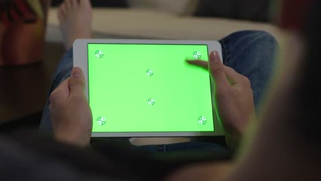 hombre joven sentado en el sofá, adolescente masculino en casa usando un dispositivo móvil para la tarea. tableta monitor de computadora pantalla verde para internet.