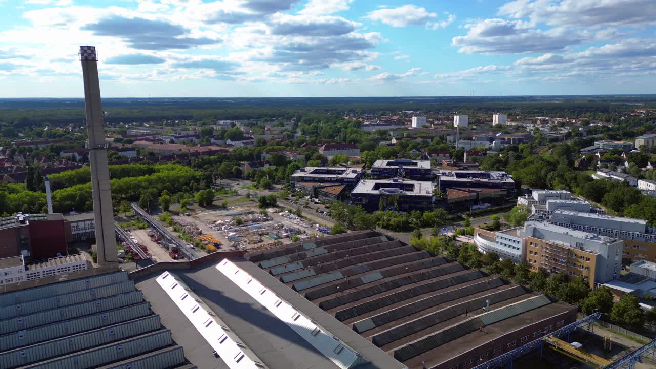 industrial buildings and a chimney in Hennigsdorf, Germany, with a train passing by. Stunning aerial view flight fly reverse drone