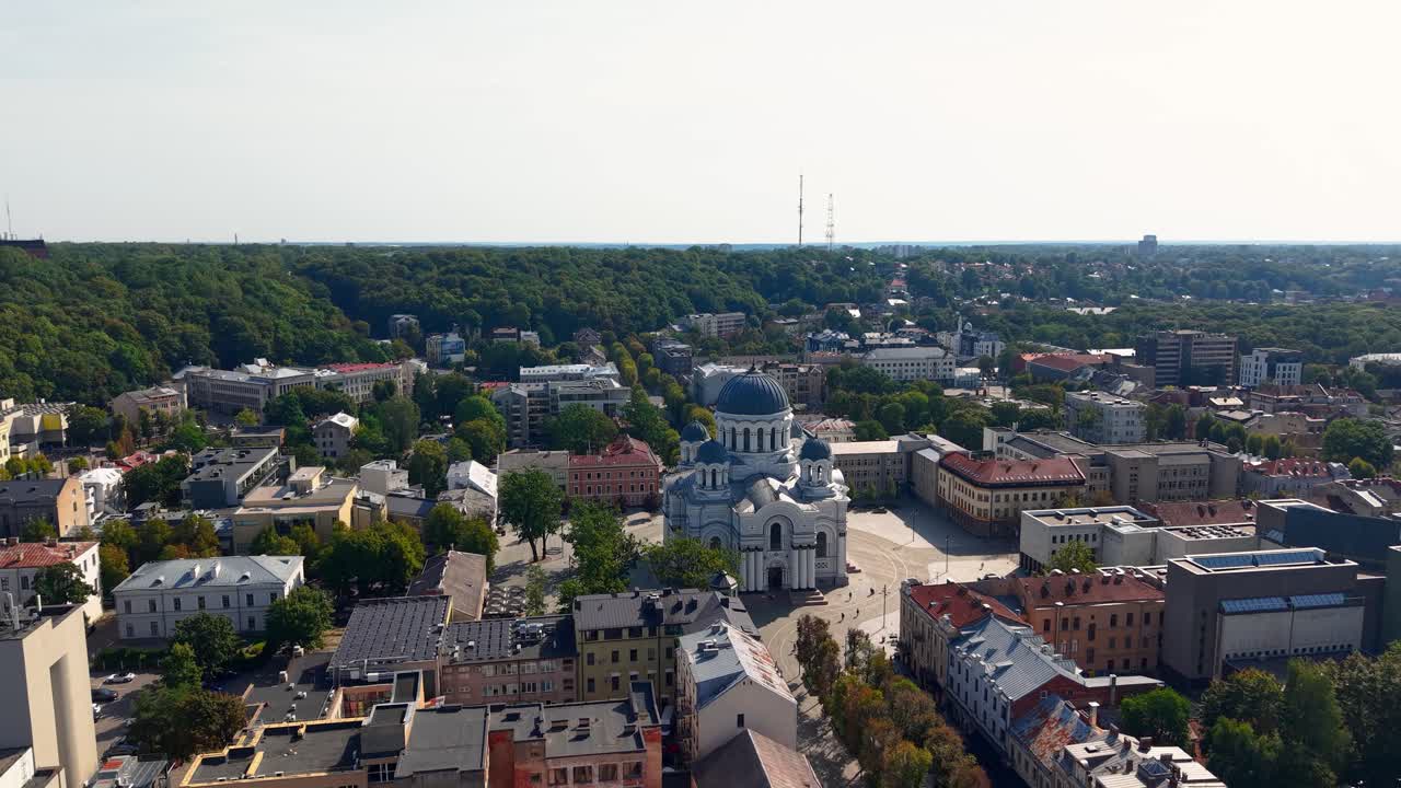 Aerial cityscape of Kaunas, Lithuania, showcasing St. Michael the Archangel Church at the end of Laisvės Alėja boulevard, surrounded by buildings and green trees on a sunny day