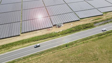 aerial drone top down shot over cars driving on road beside solar panel field on a bright sunny day