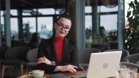 beautiful-young-woman-in-glasses-and-braces,-a-freelancer,-sits-in-a-stylish-restaurant-with-a-laptop,-dressed-in-business-attire-and-glasses,-smiling-and-posing-for-the-camera