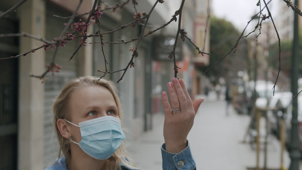 Женщина в маске любуется первыми листьями на деревьях. Приближается весна.