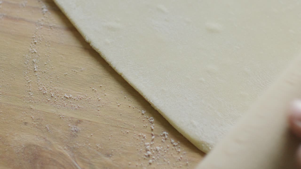 Hands Using Rolling Pin to Flatten Dough on Table Dusted with Flour