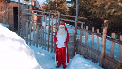 santa está de pie junto a una valla de madera y hablando con la cámara