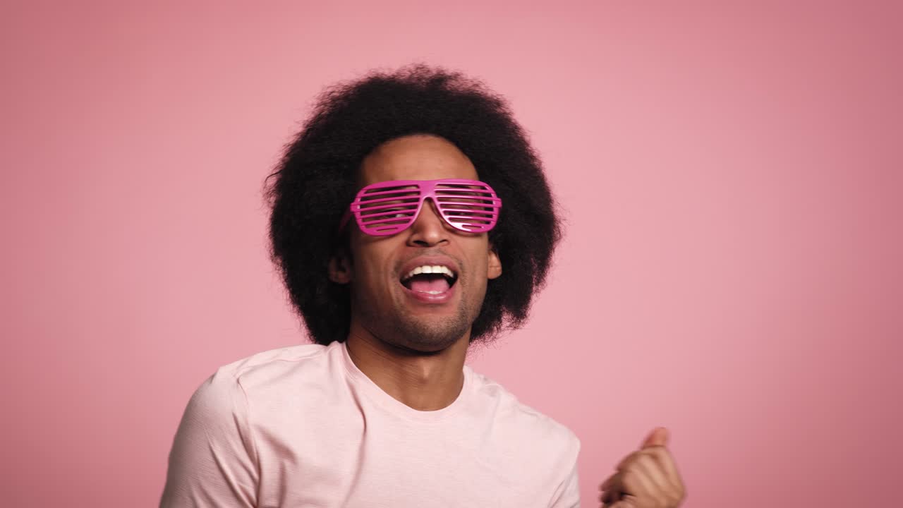Young African man smiling and dancing in the pink glasses