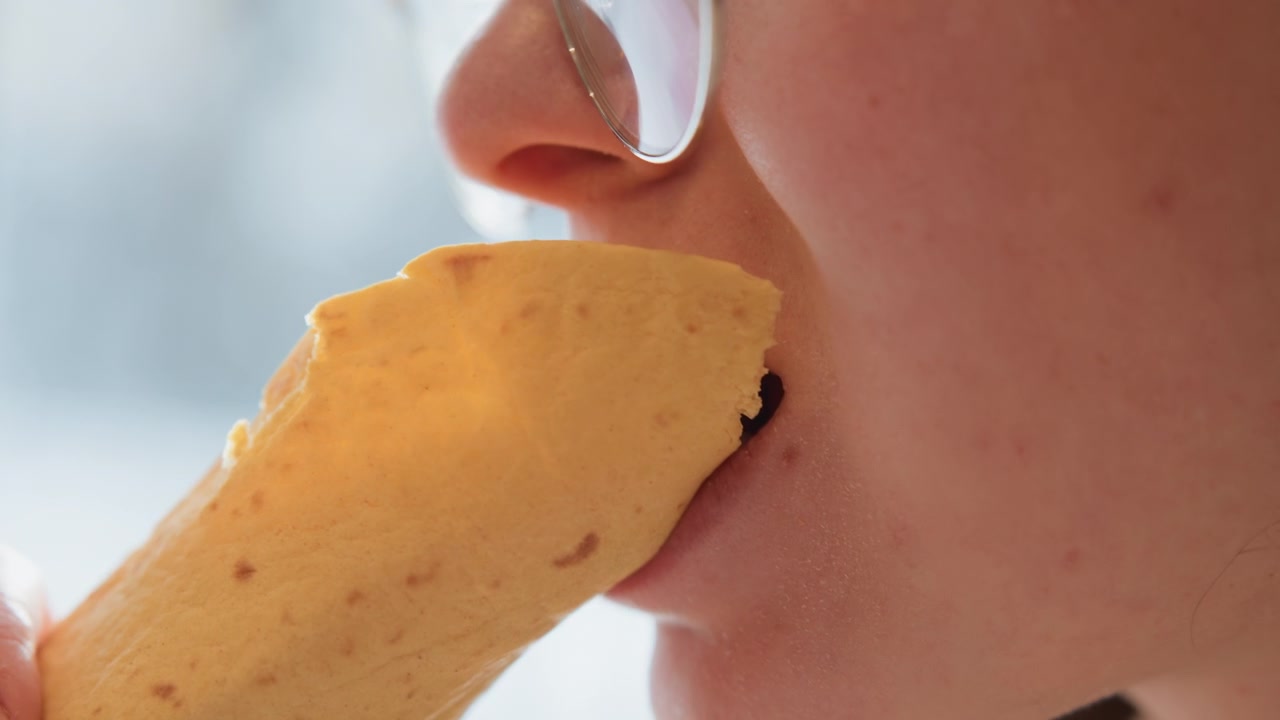 Tight close-up captures lower face moving toward handheld golden pastry, lips pursed and pastry edge near mouth, with flaky crumbs, warm light, and subtle sensory anticipation, with pastry, mouth