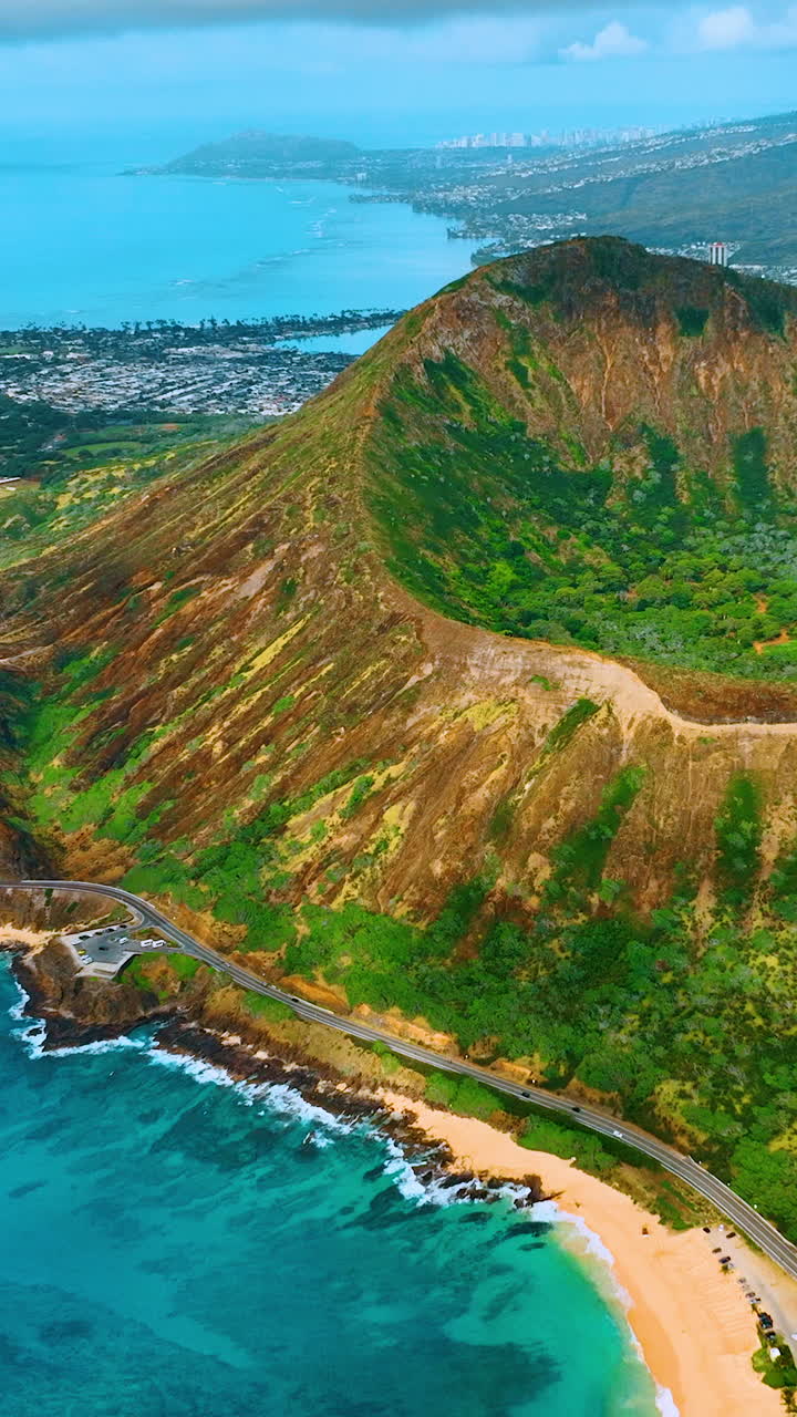 Ampia veduta di una spiaggia sabbiosa, acqua turchese, strada costiera e i pendii di un cratere vulcanico sotto un cielo blu. Panorama aereo di Sandy Beach Park e Koko Head. Video verticale.