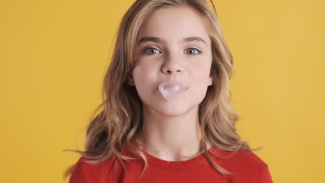 una adolescente caucásica masticando chicle y soplando burbujas.