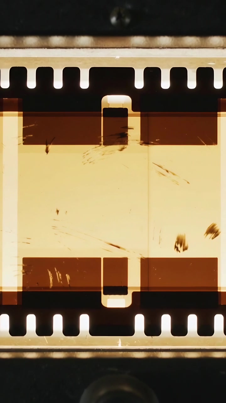 縦型動画：モーターが作動し、スプロケットで35mmフィルムストリップがゲートを通りスキャンされるために進む。