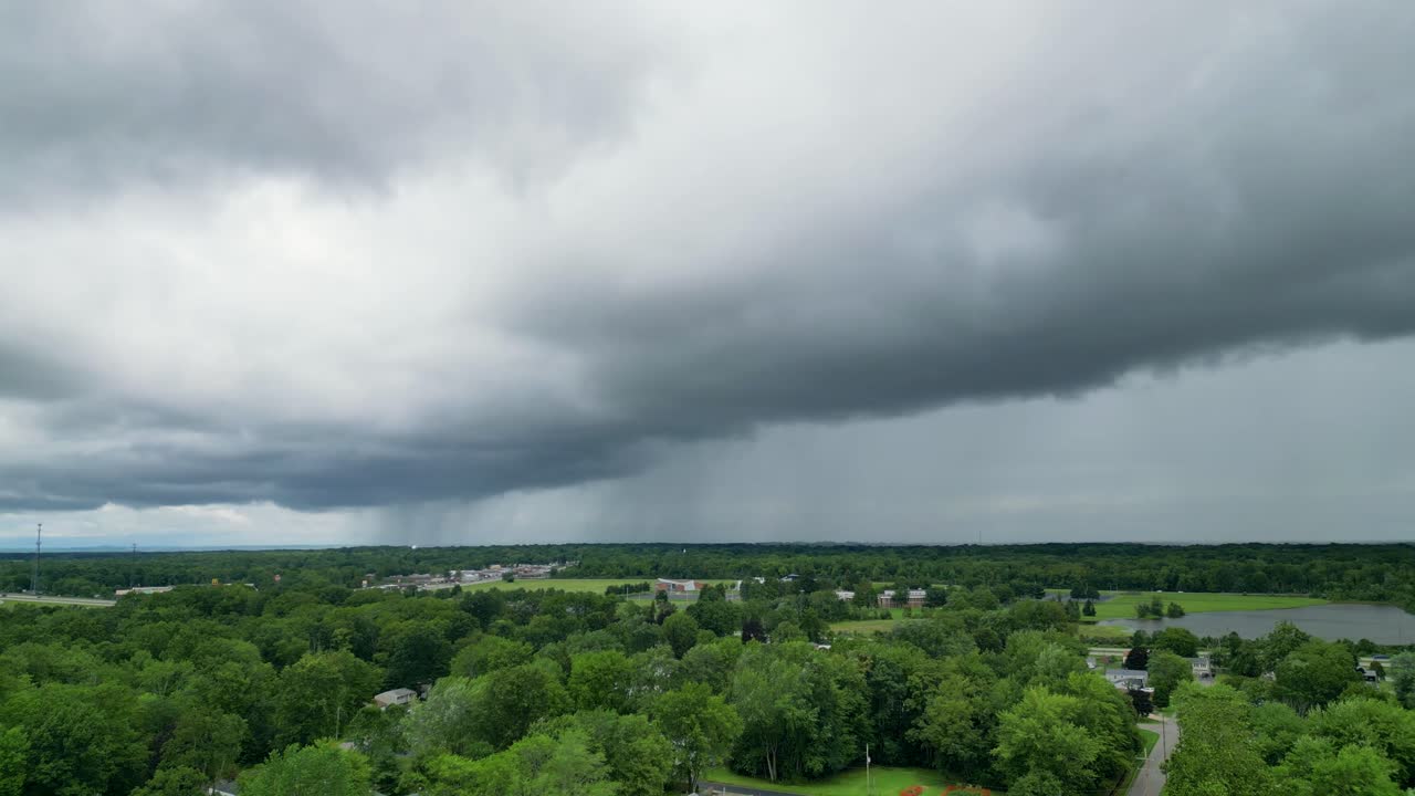 disparo de drone de nubes de tormenta ominosa rodando sobre un área suburbana con vegetación exuberante debajo