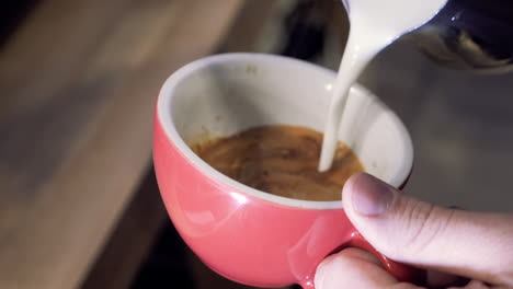 barista vertiendo café con leche en una taza roja