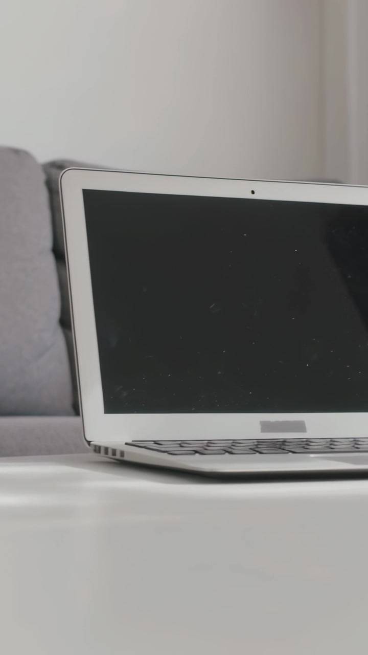 Video verticale: Telecamera che panoramica per rivelare un laptop argentato su un tavolo a casa, con tazza, spazio per il testo.