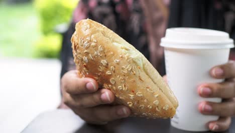 persona disfrutando de sándwich de pan de avena y café al aire libre