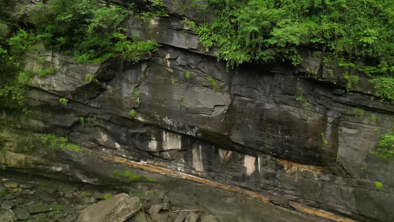 View of a stratified rock wall with scattered boulders and creeping vegetation, showcasing geological textures in a lush Philippine forest setting