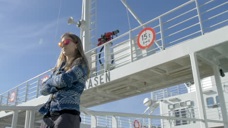 a woman in sunglasses walks along the deck of a ferry on a bright sunny day, low angle