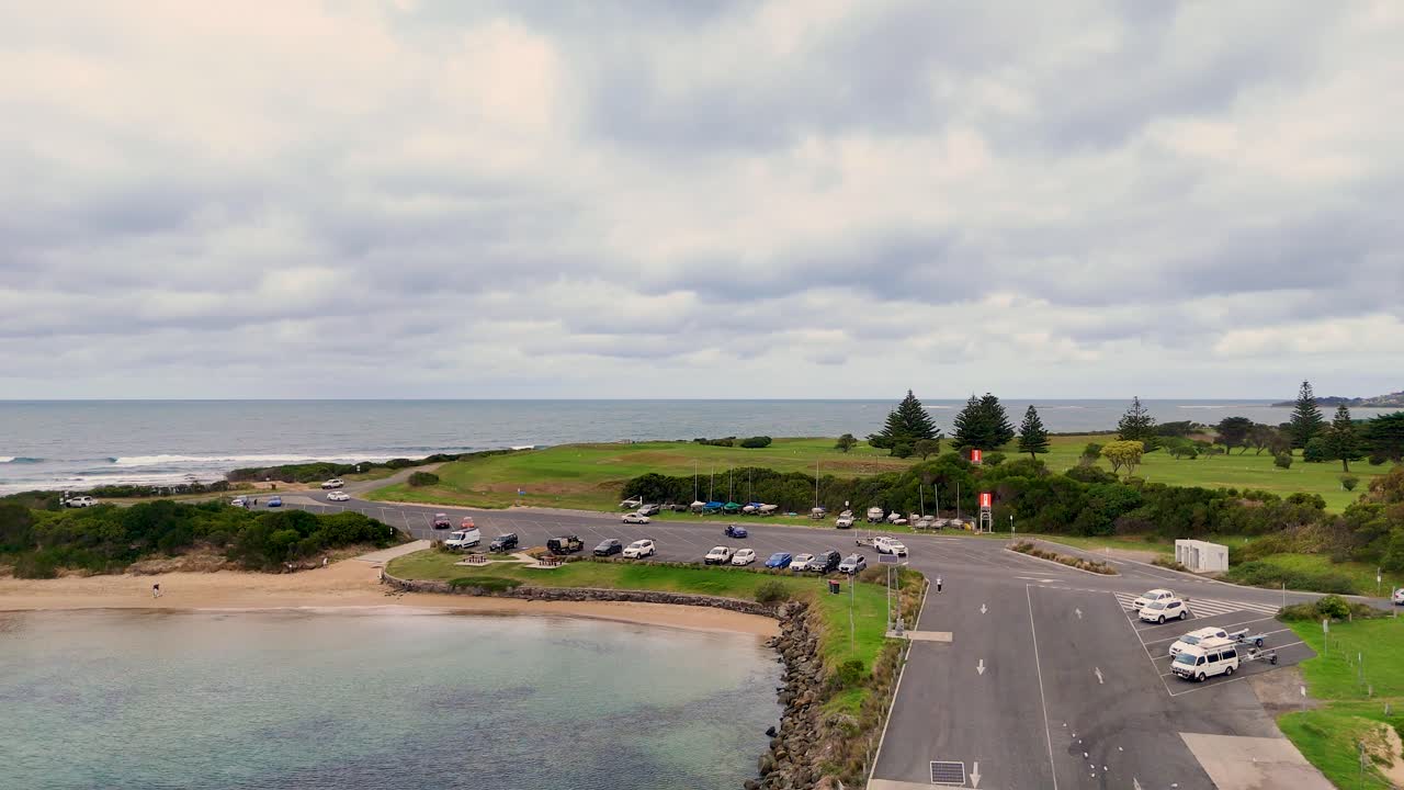 Drone footage captures Port Campbell's coastline, showcasing a jetty, parked cars, and lush greenery under overcast skies