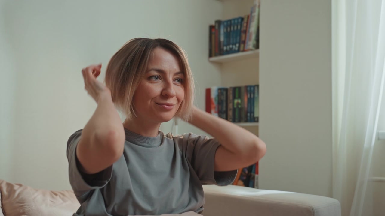 Young caucasian woman wakes to music in cozy bedroom, sits up, stretches, runs hands through hair, smiles at sunlight, glances at bookshelf, mimics singer, dances softly, daydreams about lover