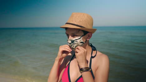 mujer joven en bikini rosa disfruta del sol en el océano tranquilo y se pone una máscara facial