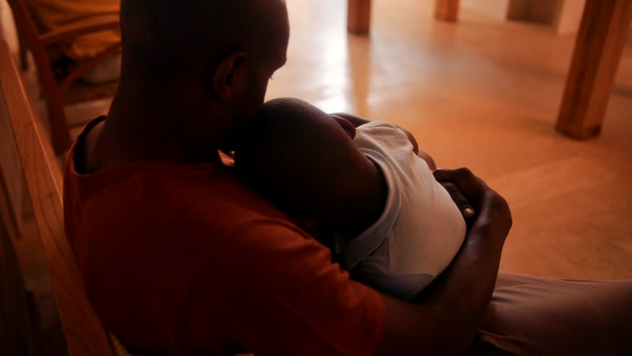 un padre amoroso acuna a su hijo pequeño para que duerma en sus brazos