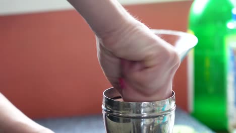 bartender twists and muddles in a silver cobbler shaker with a muddler to make a cocktail or mixed drink in a martini glass, closeup of beverage and woman’s hands tapping the edge of the glass