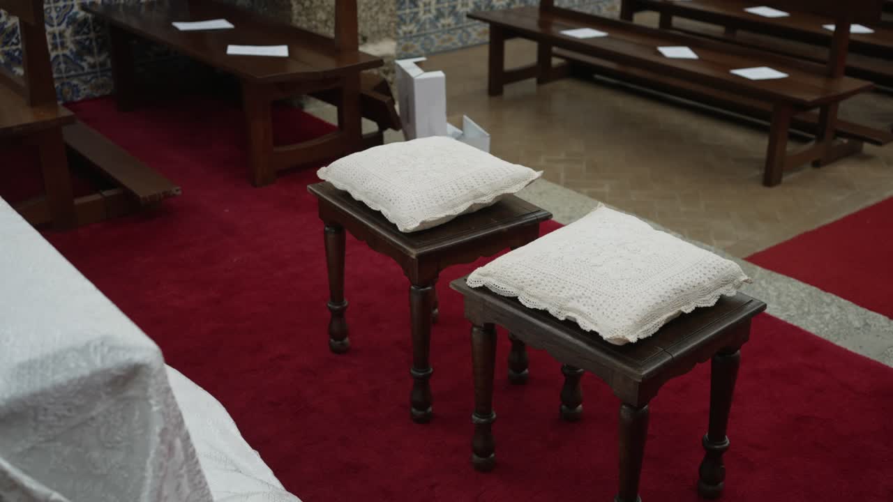 two wooden prayer stools with white crochet cushions placed in front of altar in church aisle