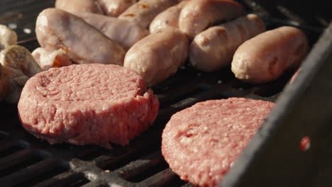 chef placing raw beef burgers on bbq with pork sausages and shish kebabs with heat and smoke rising