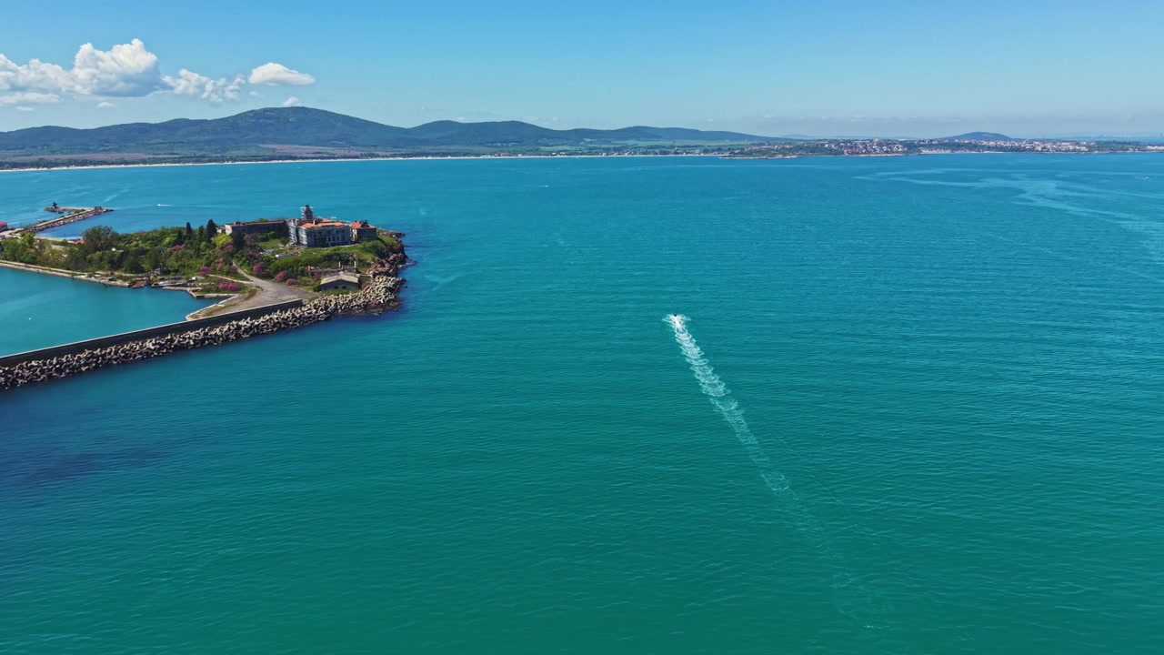 Panorama costiero che mostra acqua, imbarcazioni e colline distanti, con tempo soleggiato, vicino a una città lungo la riva in un'area costiera.