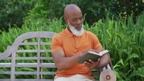 un anciano afroamericano leyendo un libro mientras está sentado en un banco en el jardín