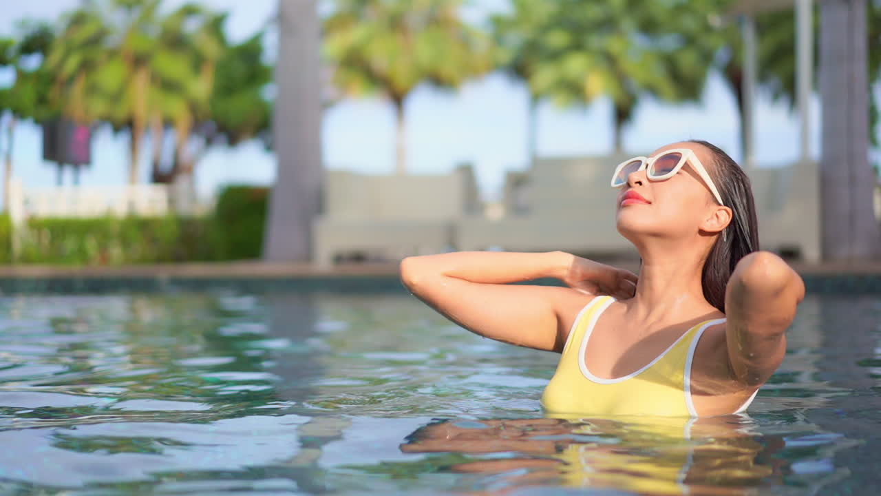 サングラスと黄色の水着を着た少女が、プールで濡れた髪をなでる