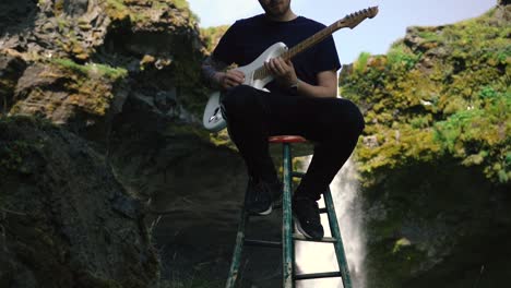 hombre tocando la guitarra frente a una hermosa cascada en islandia-2