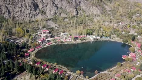 Hermoso-Paisaje-Aéreo-De-árboles-De-Otoño-Y-Lago-Con-Cabañas-Rojas